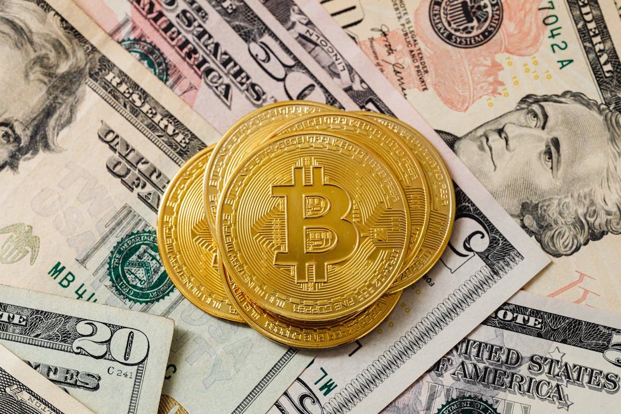 Home Close-up of gold bitcoin coins on US paper money, representing cryptocurrency investment.